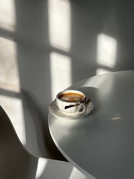 Elegant coffee cup casting shadows on a minimalist table, bathed in natural light.