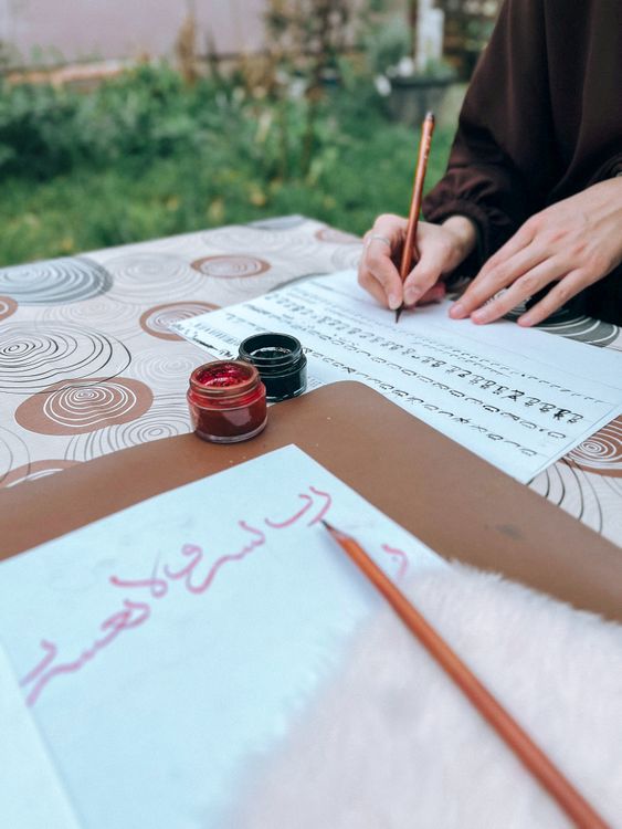 Person Practicing Calligraphy Outdoors on Paper · Free Stock Photo