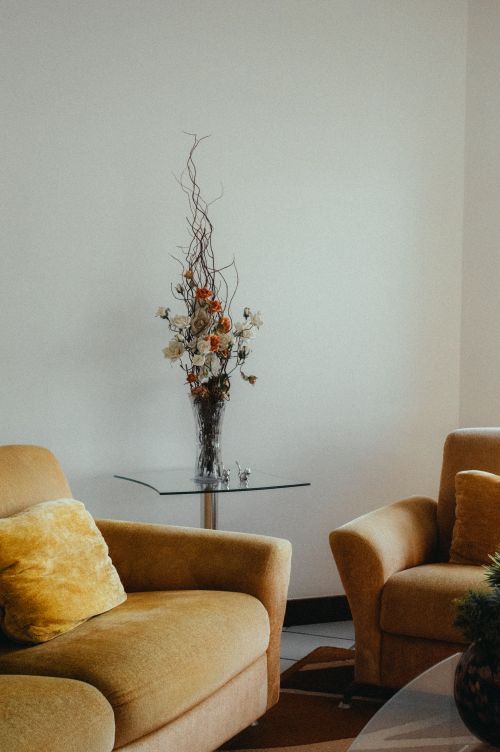 Free Warm living room interior featuring beige armchairs and a tall floral vase on a glass table. Stock Photo