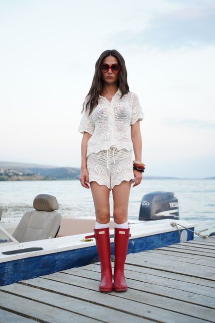 Fashionable woman in red boots standing on dock by the sea, exuding modern coastal style.