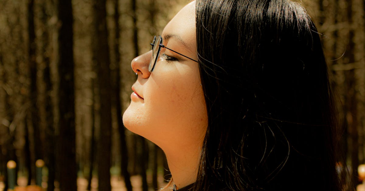 Profile of a woman standing peacefully in a sunlit forest with closed eyes.