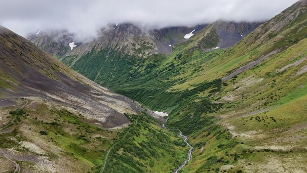Breathtaking view of lush green mountain valley with cloud-covered peaks.