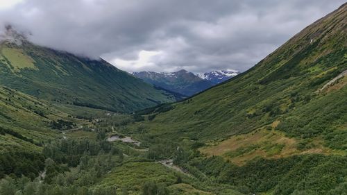 Free A scenic view of a lush green valley surrounded by majestic mountains under a cloudy sky. Stock Photo