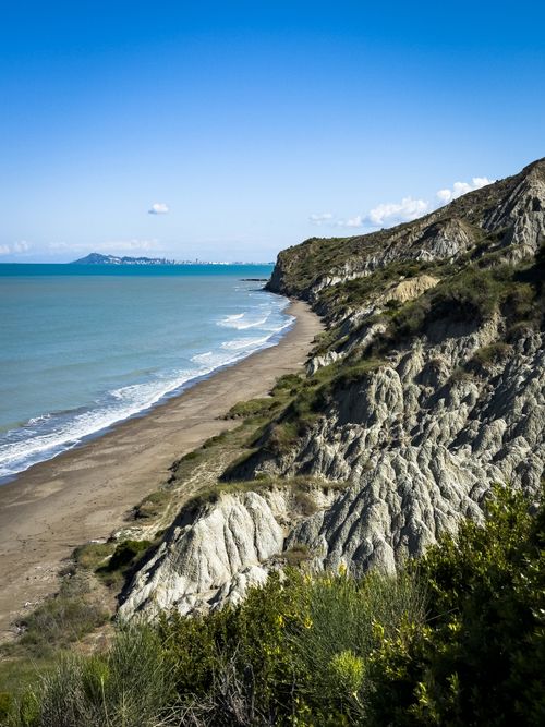 Free Exploring rugged cliffs and a serene coastal beach under a clear blue sky. Stock Photo