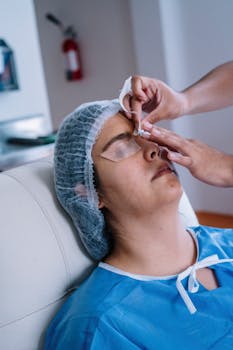 A patient undergoing eye surgery preparation, wearing protective clothing and hair covering.