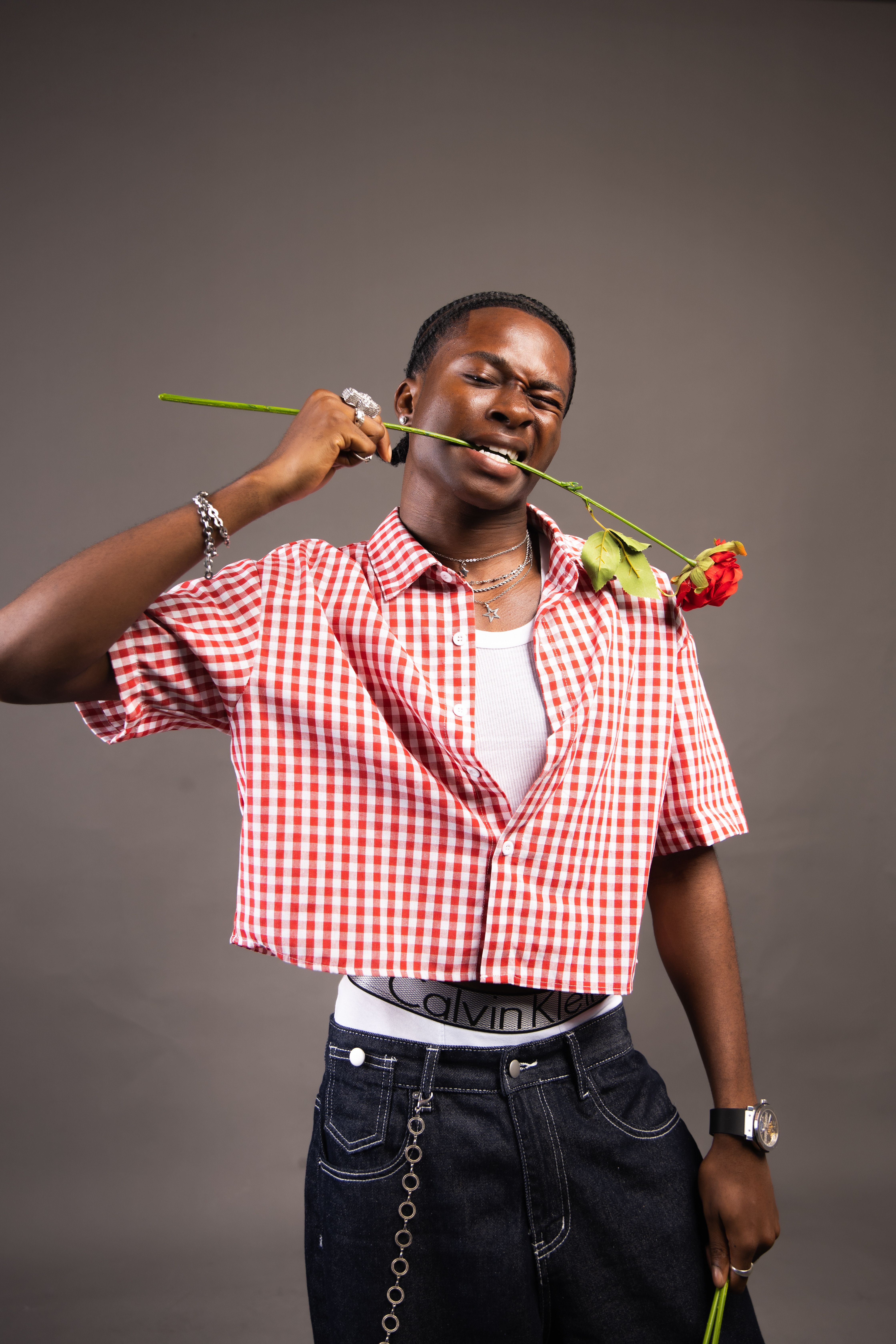 Young man in modern attire holding a rose, photographed in studio.