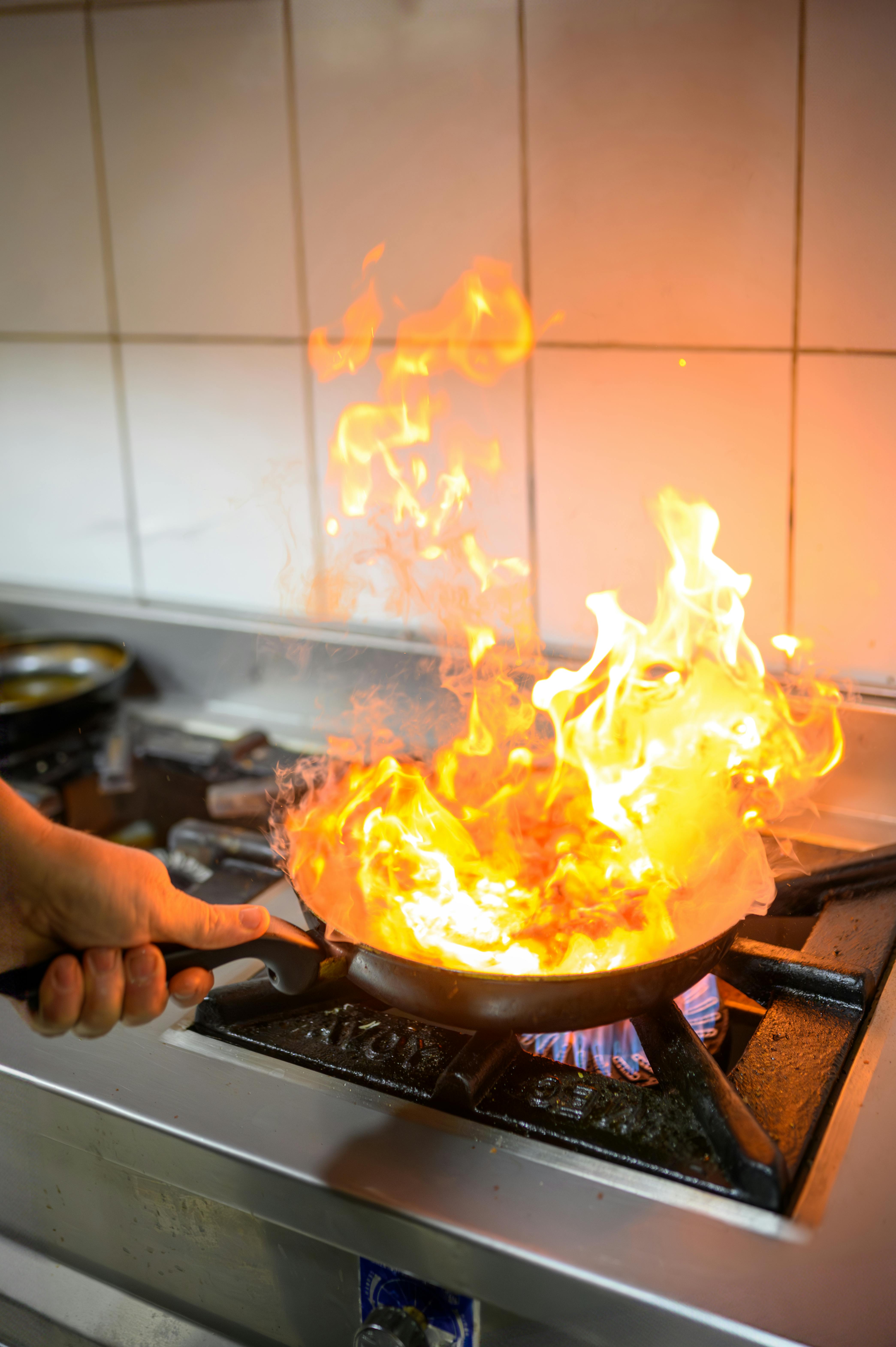 Vibrant flames from a pan on a gas stove, showcasing culinary skill in a professional kitchen.