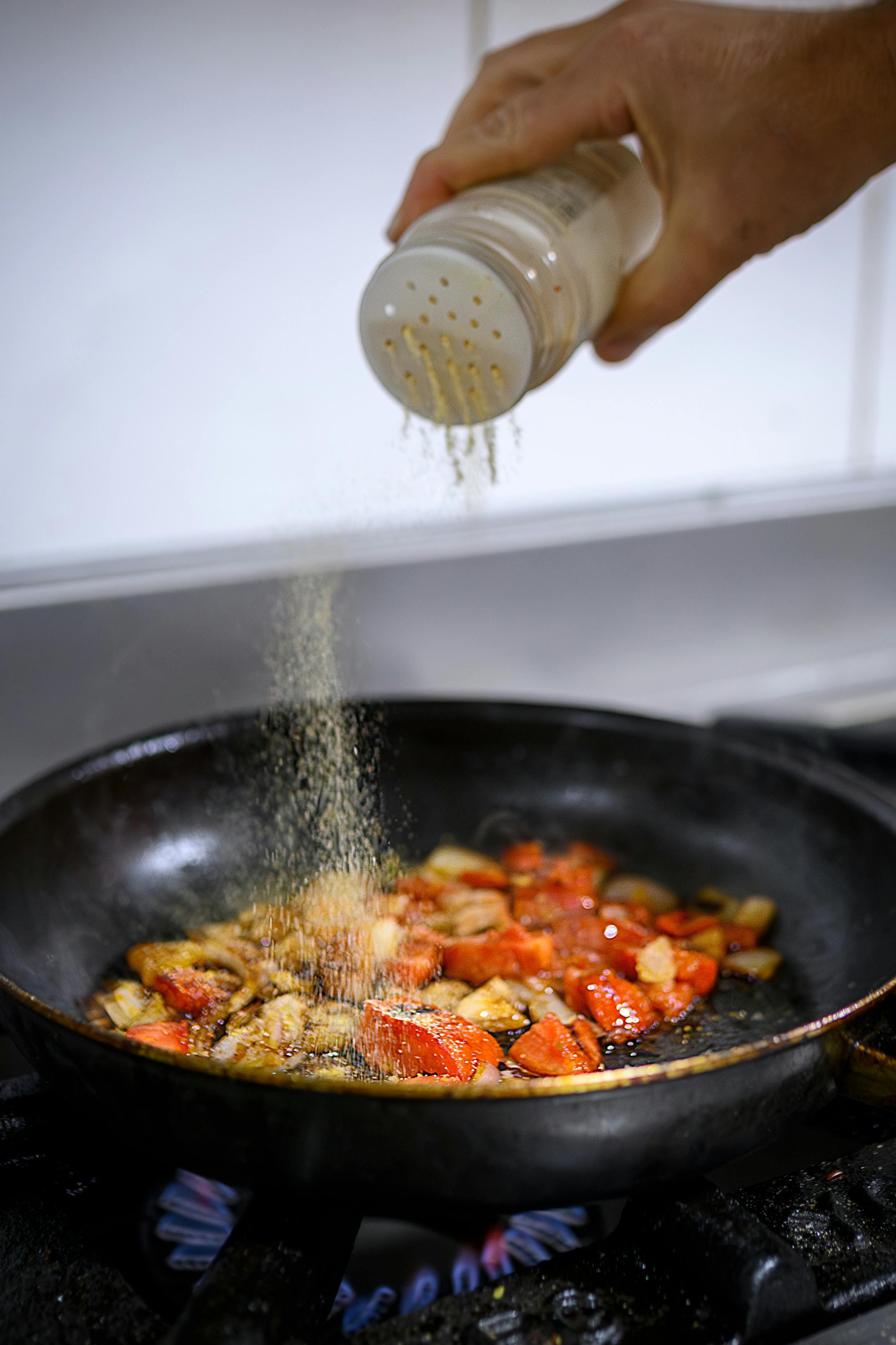 Mano dello chef che spolvera spezie colorate su verdure saltate in padella