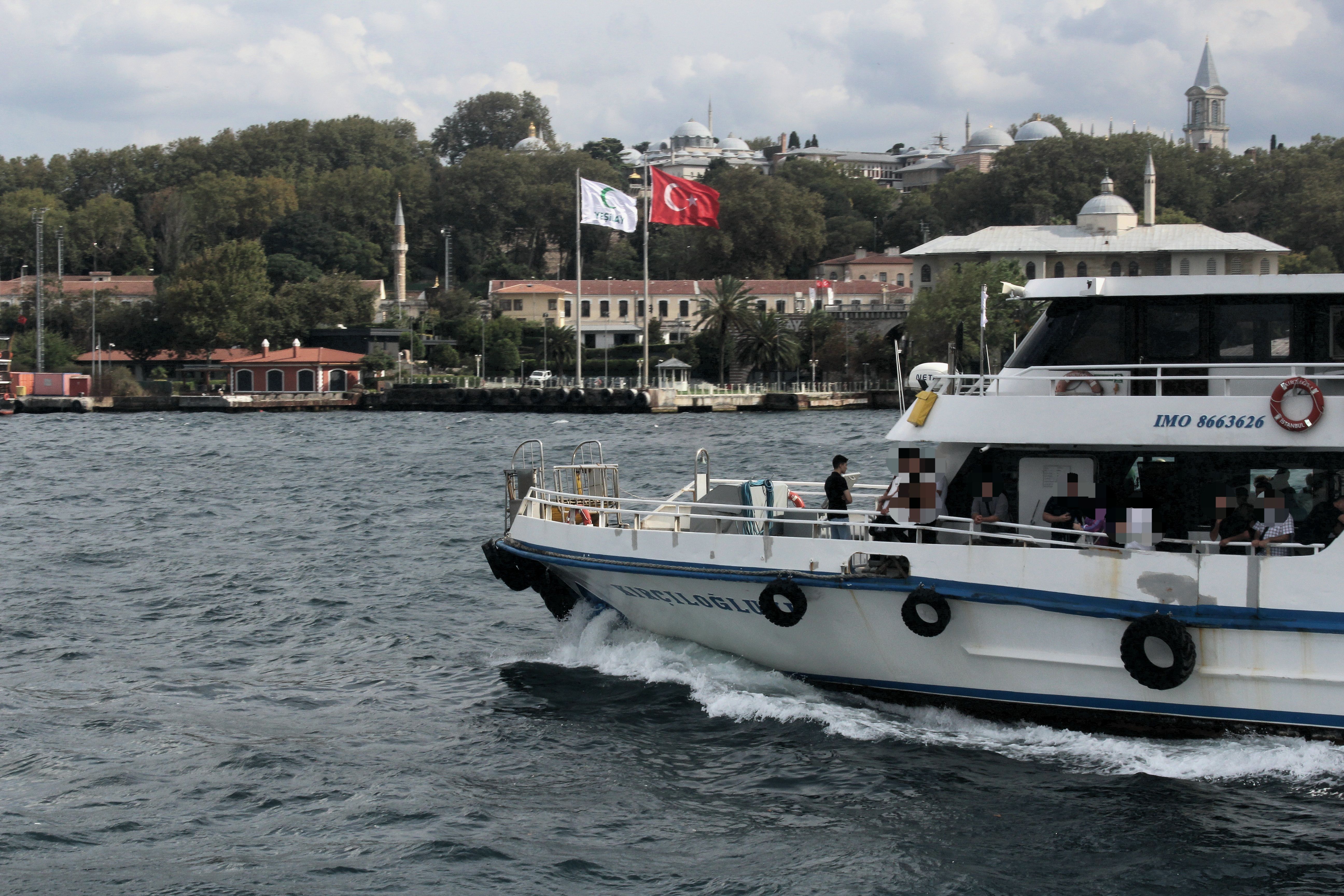 Ferry sailing on the Bosphorus with Istanbul landmarks and Turkish flag in the background.