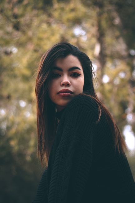 Moody portrait of a young woman with long hair, wearing a sweater, in a forest setting.
