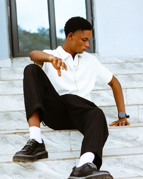 Free Young man in fashionable attire sitting on marble stairs outdoors, wearing a smart watch. Stock Photo