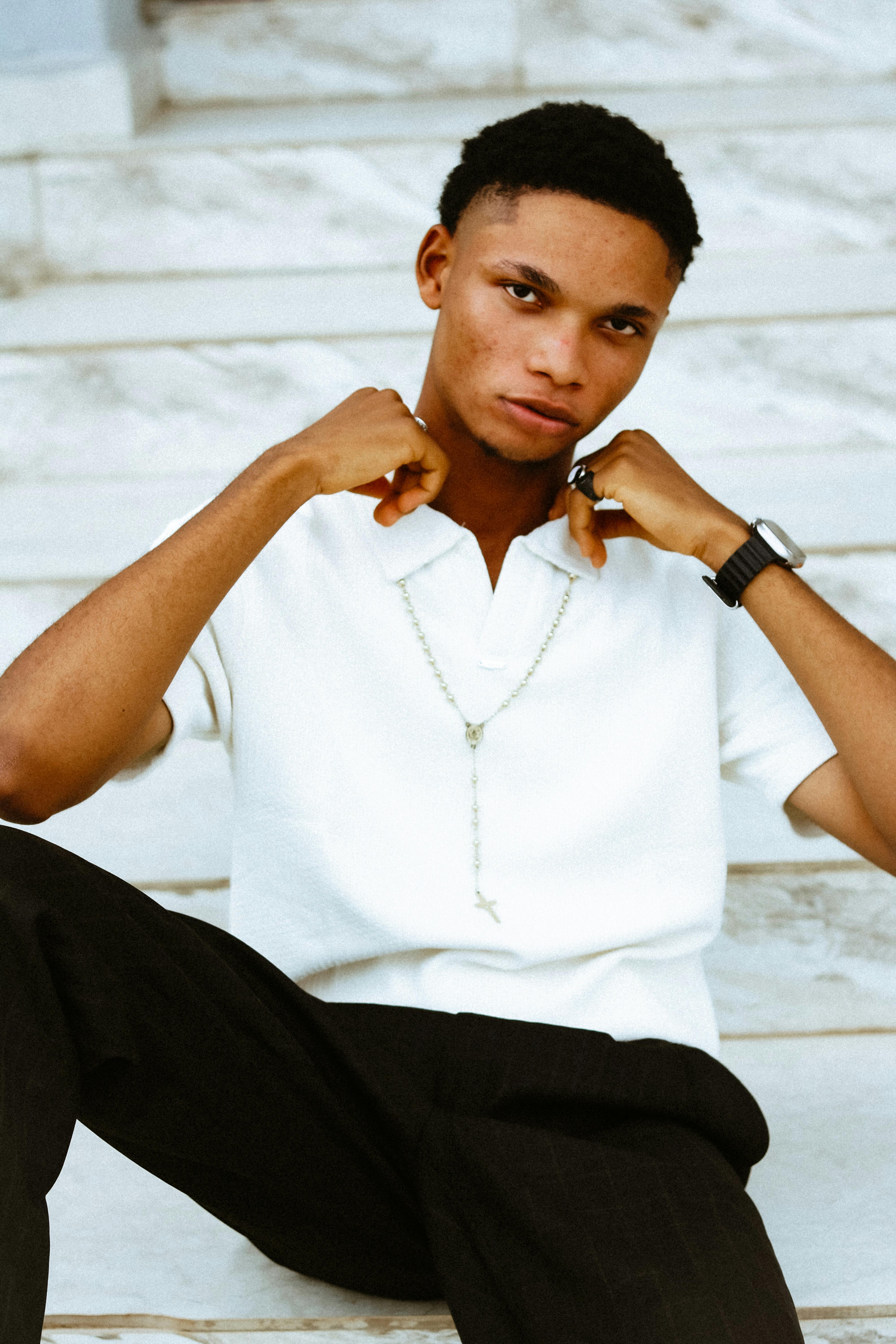 Confident young man posing on steps with modern style in a white shirt.