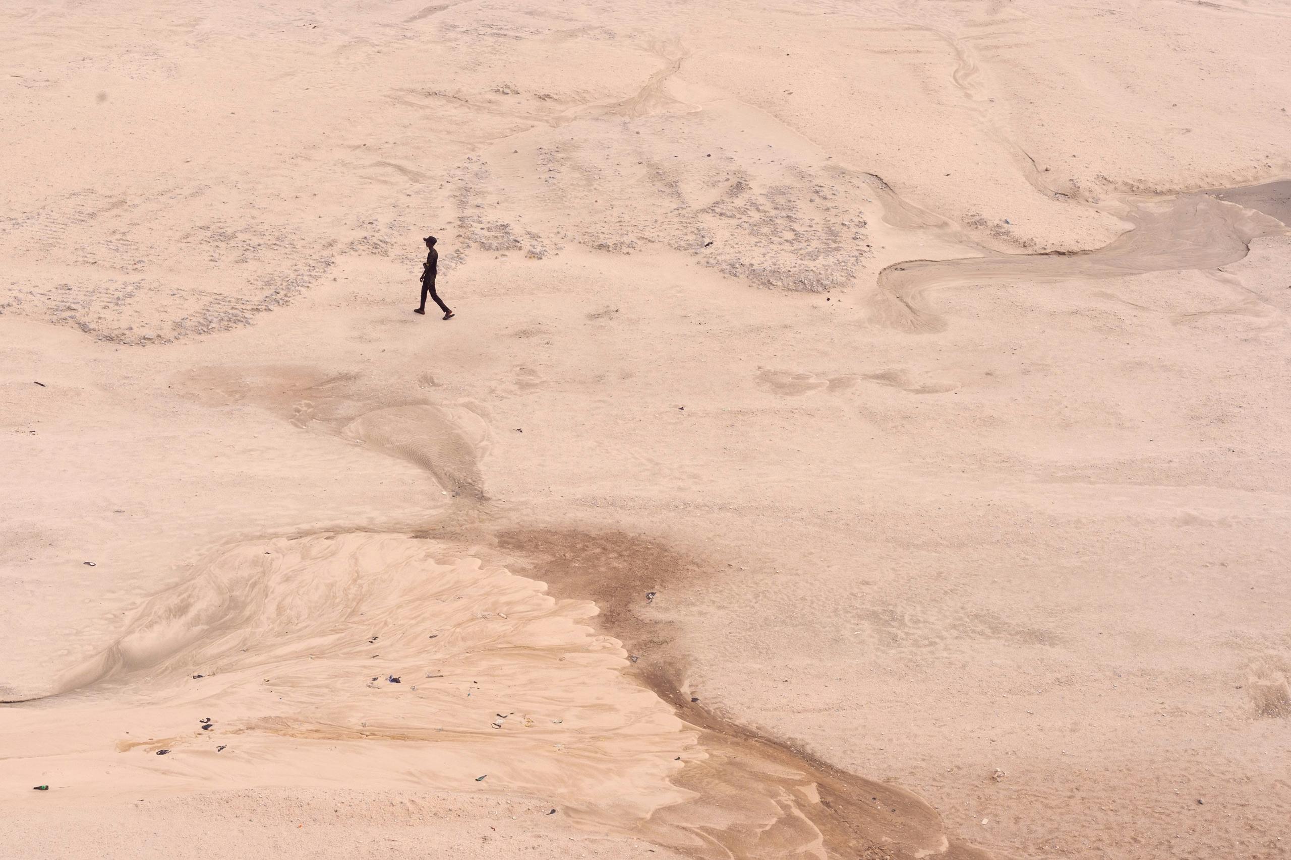 A solitary person walks across a vast, empty desert expanse, suggesting isolation and vastness.