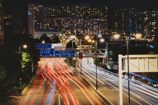 Dynamic city highway at night with vivid vehicle light trails and illuminated skyscrapers in urban setting.