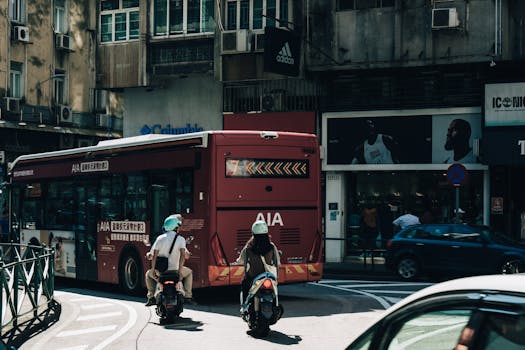Dynamic street view capturing two scooter riders trailing a bus in bustling Macau city.