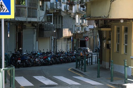 Street scene in Macau showing parked motorcycles and residential buildings in a narrow alley.