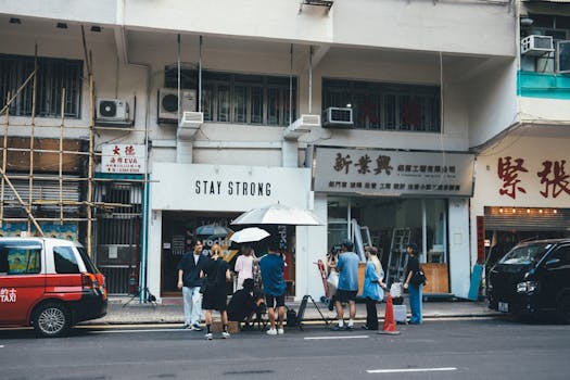 Group of people gather outside the Stay Strong store on a busy city street in daylight.