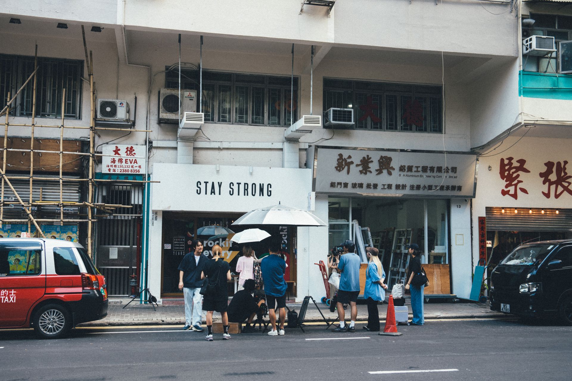 Group of people gather outside the Stay Strong store on a busy city street in daylight.