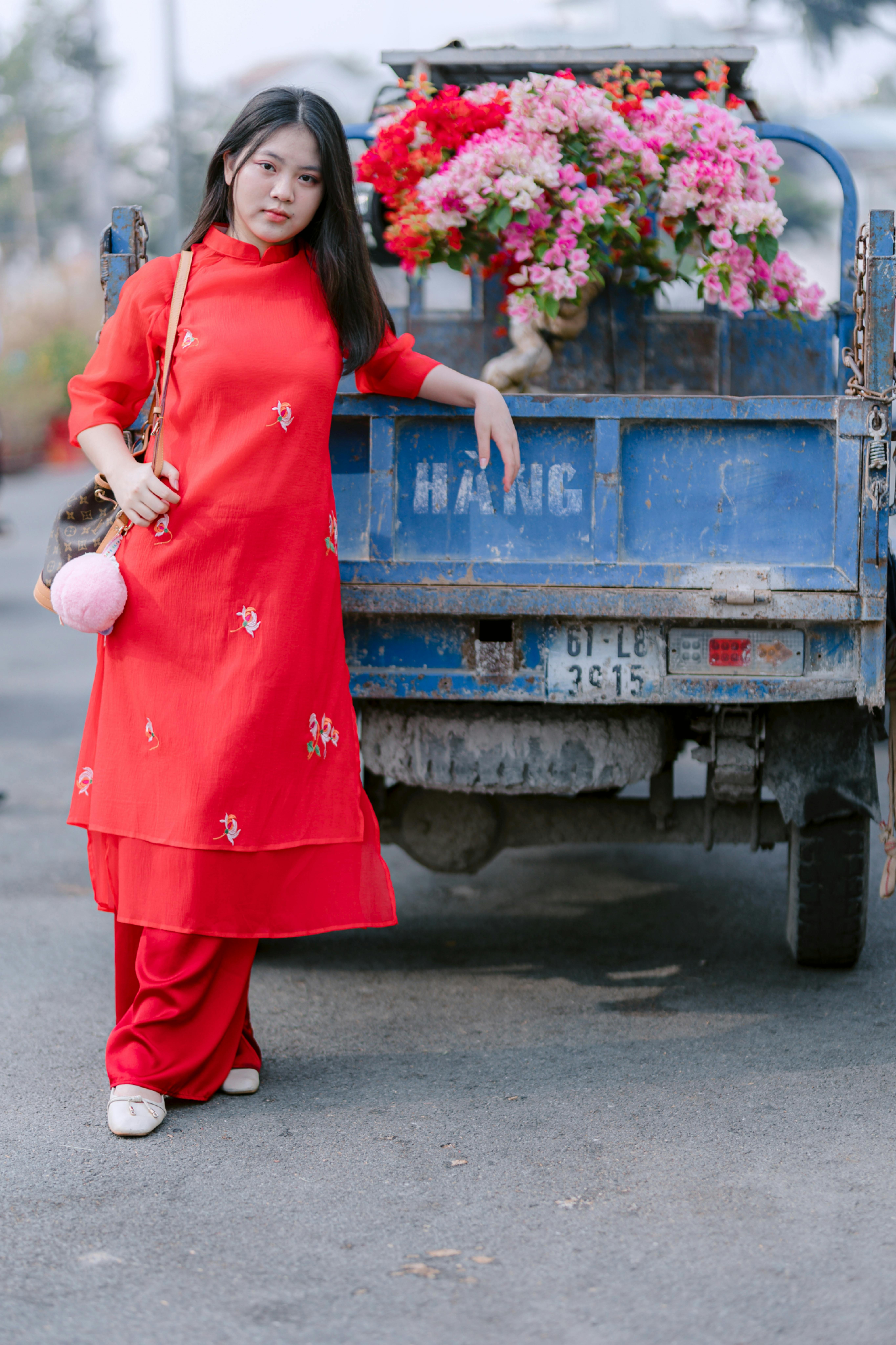 Free A stylish young woman poses by a blue flower truck in a vibrant red dress. Stock Photo