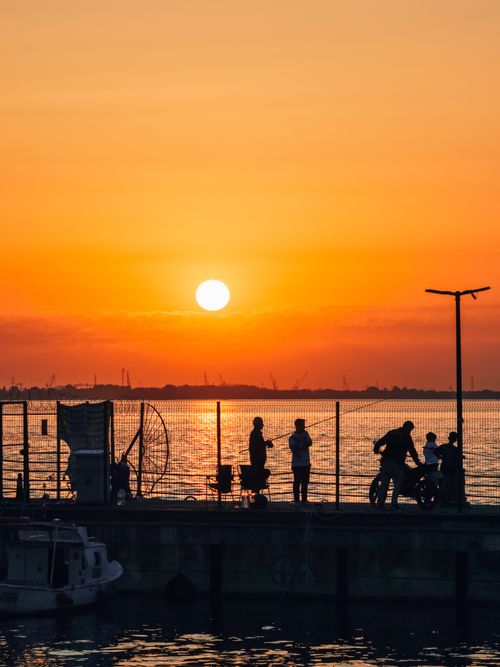 Free People enjoying a vibrant sunset by the ocean with silhouettes and warm colors. Stock Photo