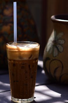 A glass of iced coffee with a straw, casting shadows in bright outdoor sunlight.