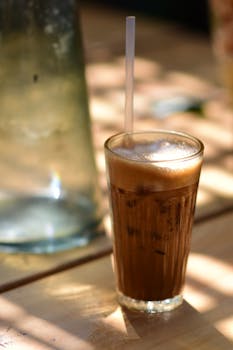Chilled iced coffee with frothy top in a sunlit setting, perfect for a summer day.
