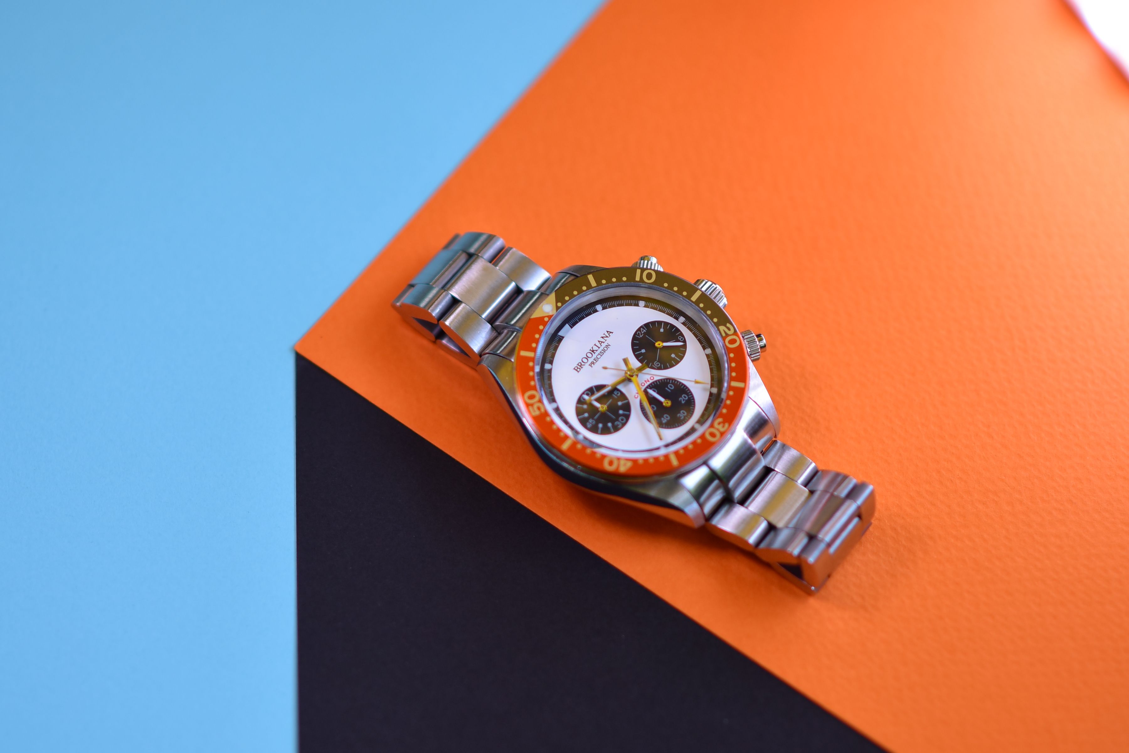 Stylish stainless steel wristwatch with orange accents on a vibrant geometric paper background.