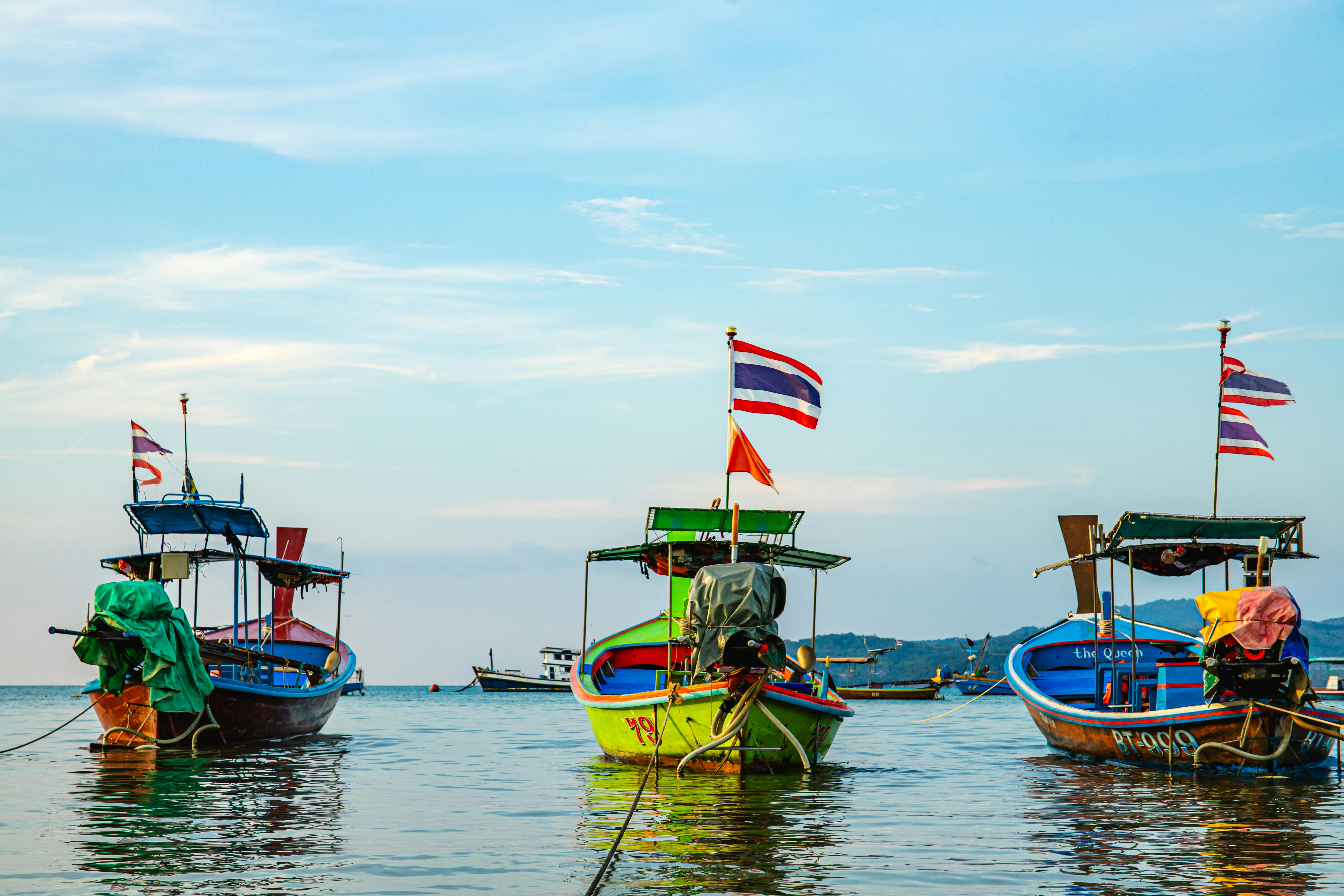 Colorful fishing boats with Thai flags anchored in the serene waters of Phuket, Thailand. - Phuket