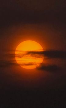 Silhouetted clouds partially obscure a vibrant sunset, creating a dramatic view.