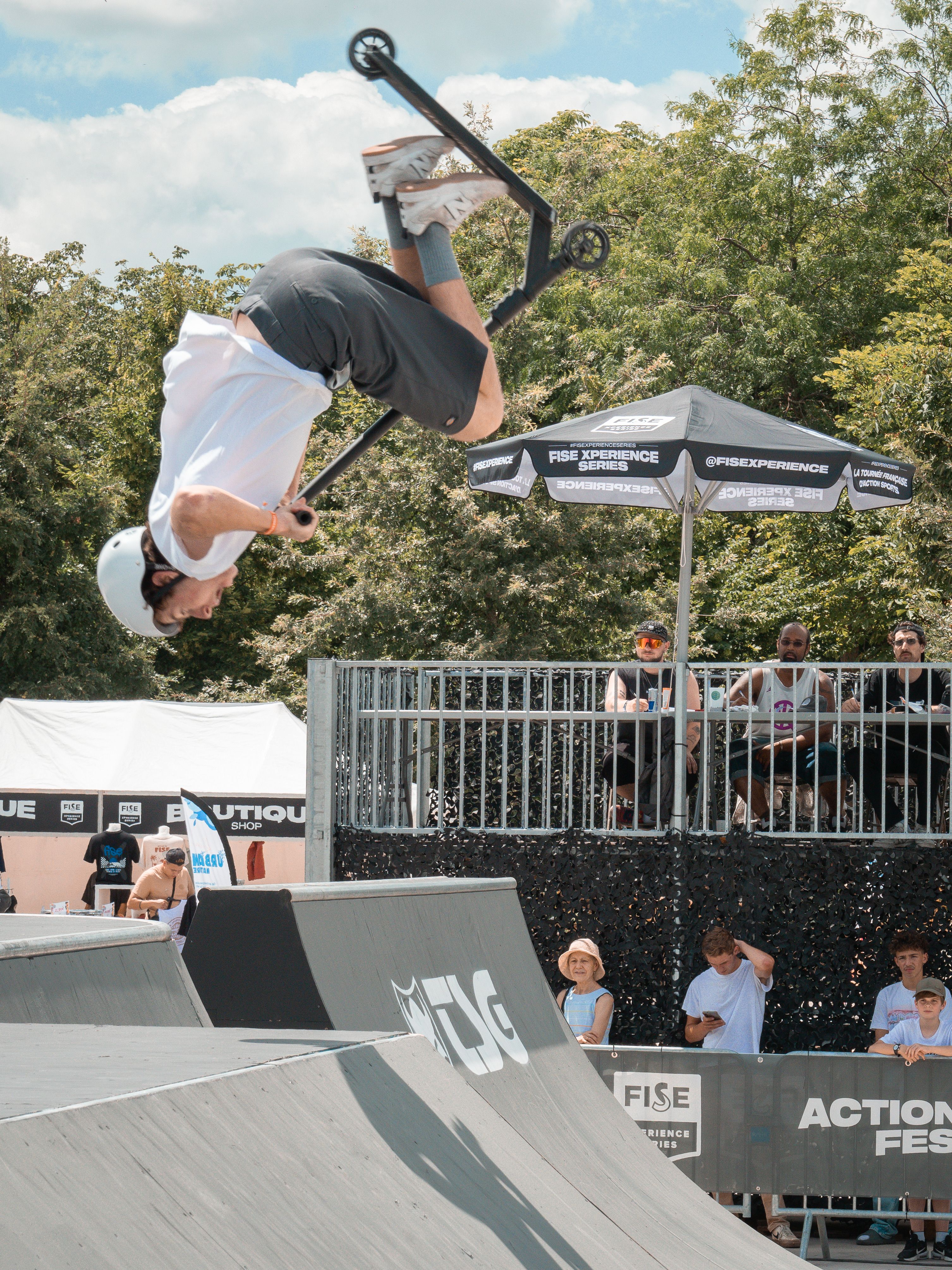 Young male performing thrilling scooter flip mid-air at an outdoor sports festival.