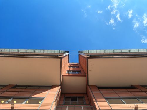 Free Low-angle view of a modern building facade with a clear blue sky backdrop and minimal clouds. Stock Photo