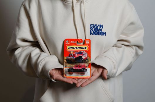 Person in hoodie holding a Matchbox toy Jeep package. Close-up, studio shot.