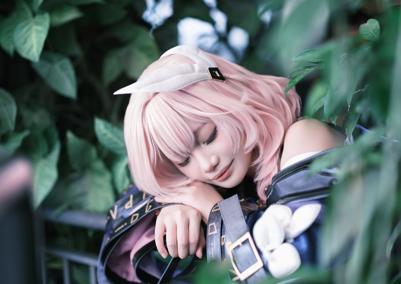 a cosplayer with pink hair rests among lush green foliage outdoors