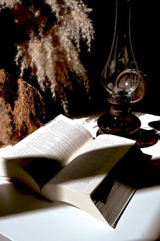 Aged book and classic oil lamp on a table with soft light creating a vintage and cozy ambience.