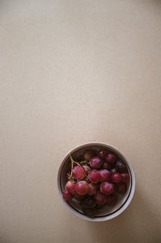 A bowl of fresh red grapes placed on a smooth beige surface, creating a simple and modern composition.