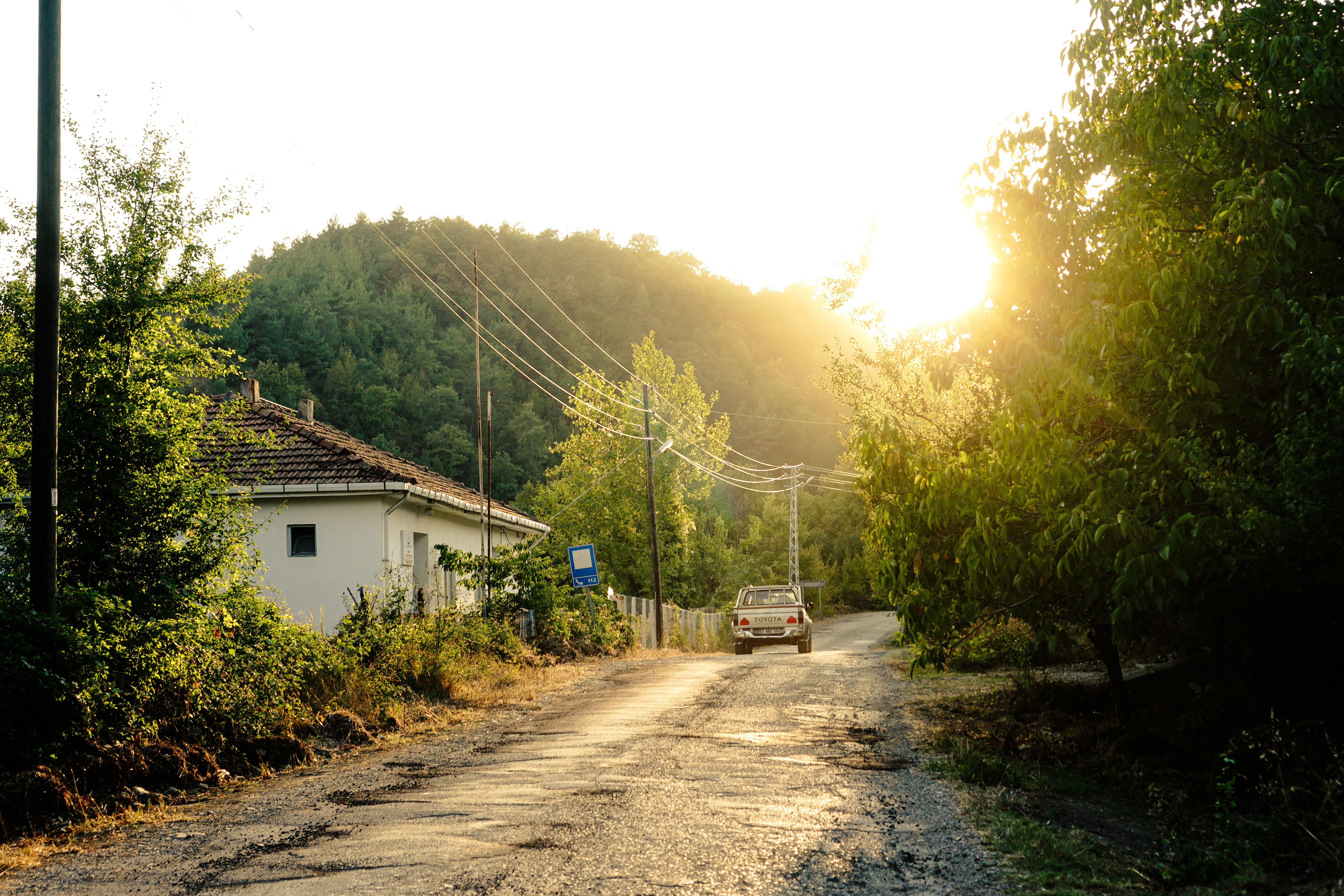 Scenic rural road with house and car at sunset, serene countryside view.