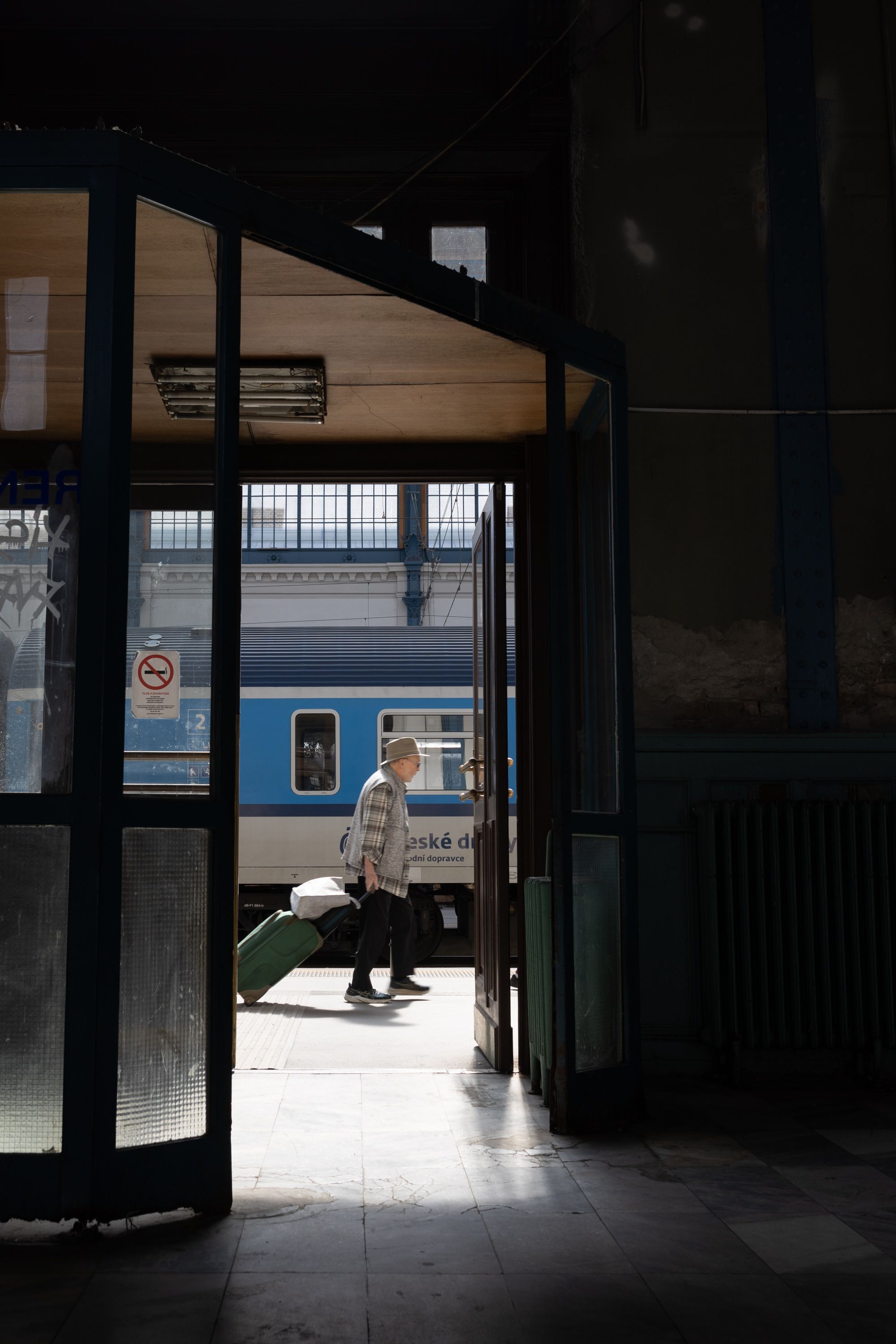 A man walks through a train station doorway, pulling a suitcase with a train in the background.