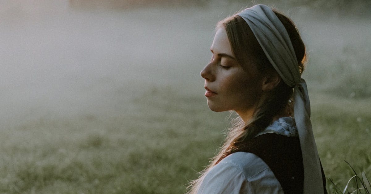 A serene woman in traditional clothes meditates outdoors at sunrise amidst misty fields.