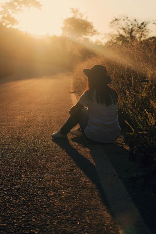 Free A dramatic silhouette of a person sitting peacefully on a sunlit road during twilight. Stock Photo