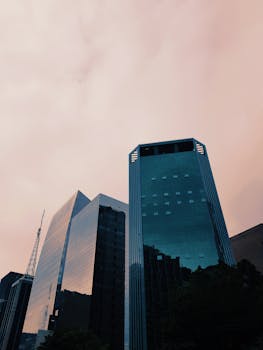 从低角度仰望，高耸的玻璃摩天大楼映照着金融区多云的天空