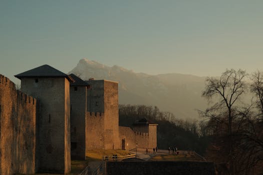Captivating view of castle walls in Salzburg, Austria, with a sunset backdrop and mountainous landscape.