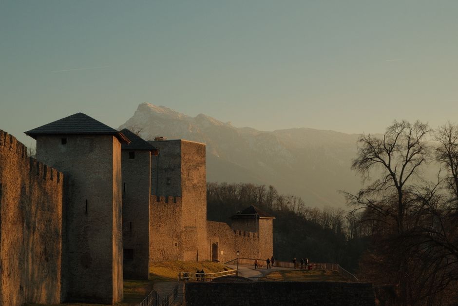 Captivating view of castle walls in Salzburg, Austria, with a sunset backdrop and mountainous landscape.