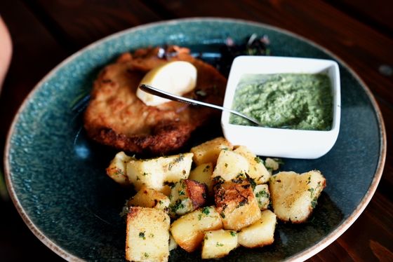 Golden pork schnitzel with egg, roasted parsley potatoes and a dish of green herb sauce