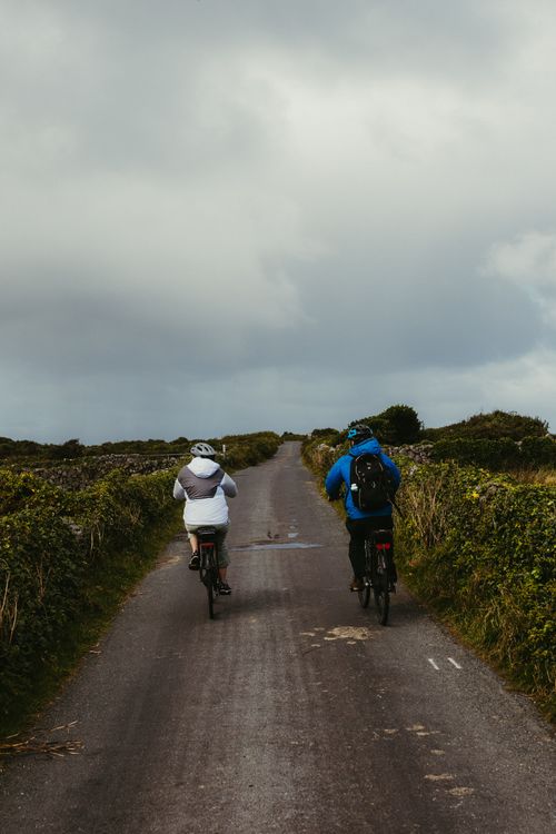 Free Two cyclists enjoy a scenic ride on a rural road in County Galway, Ireland, surrounded by nature. Stock Photo