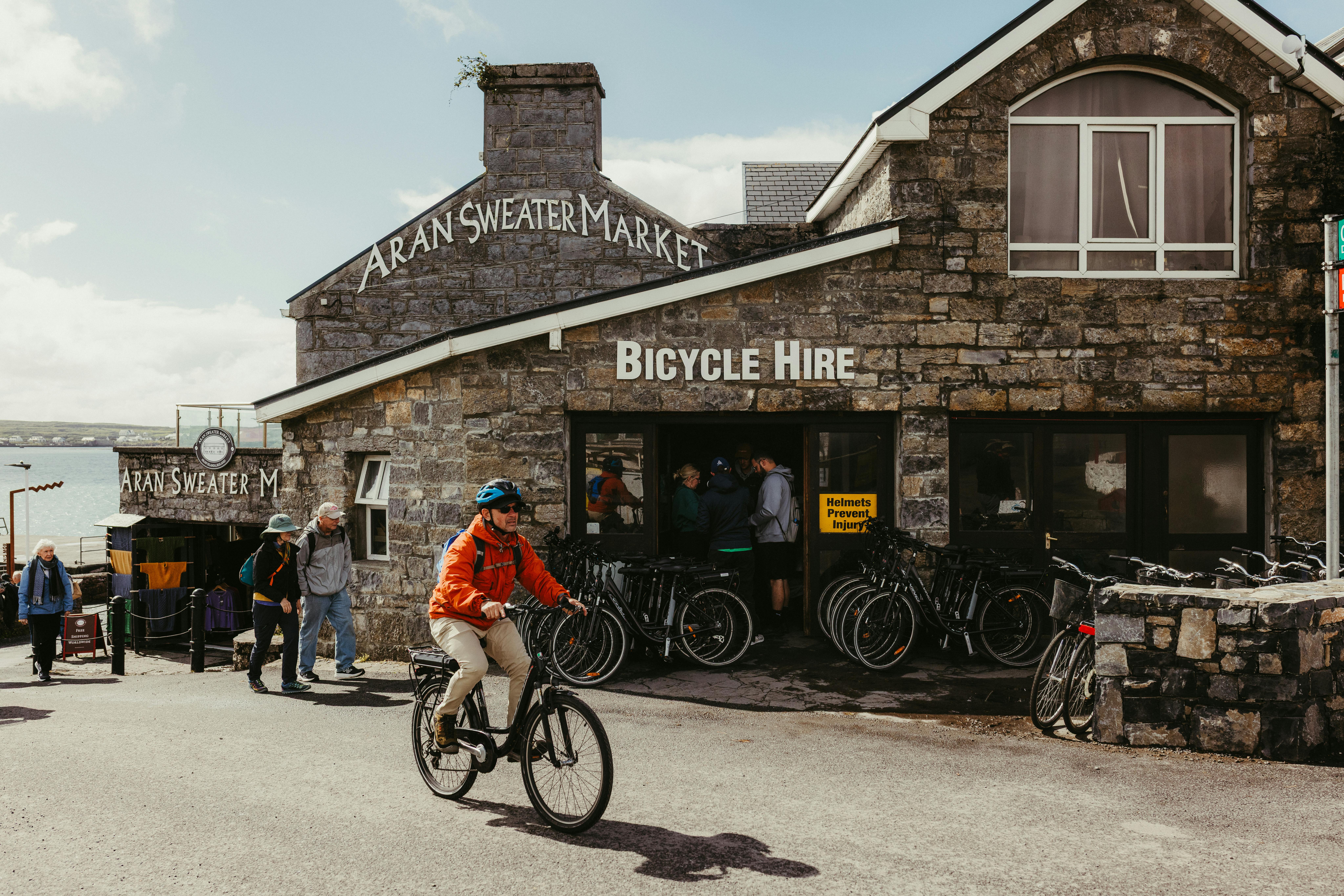 A cyclist passes the Aran Sweater Market on Inishmore, Ireland, with bicycle hire in view.