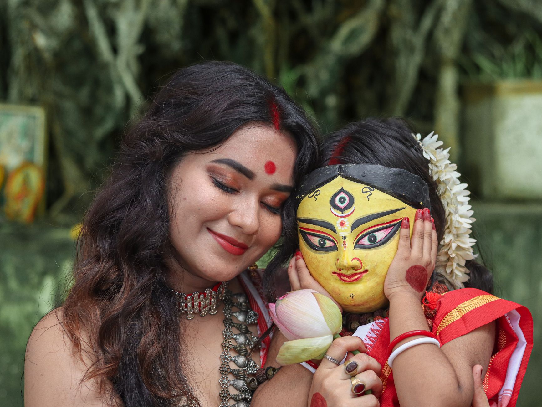 A mother and child embrace during a Durga Puja celebration, with the child wearing a traditional mask.
