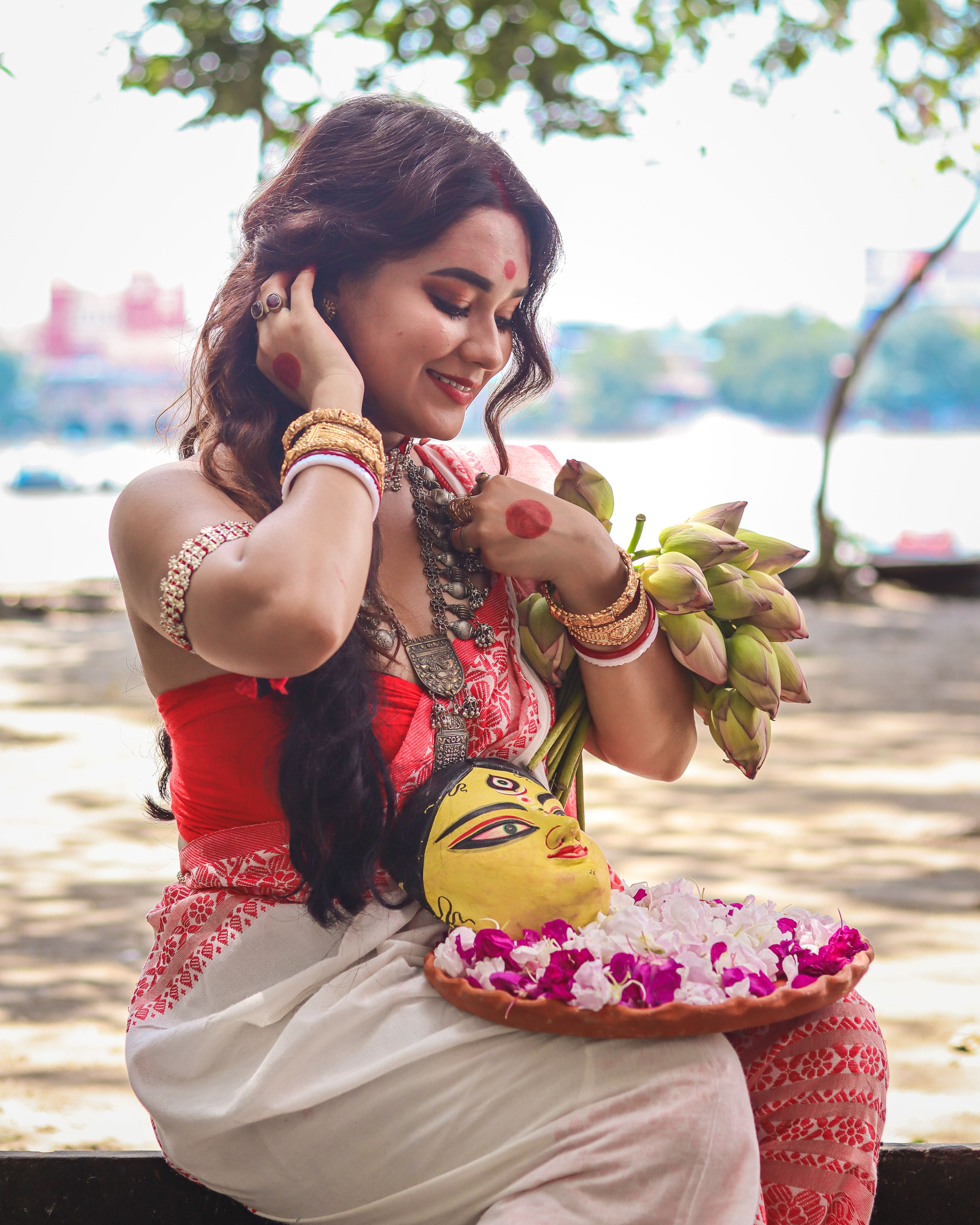 Elegant woman in traditional attire holding lotuses and decorative plate outdoors.