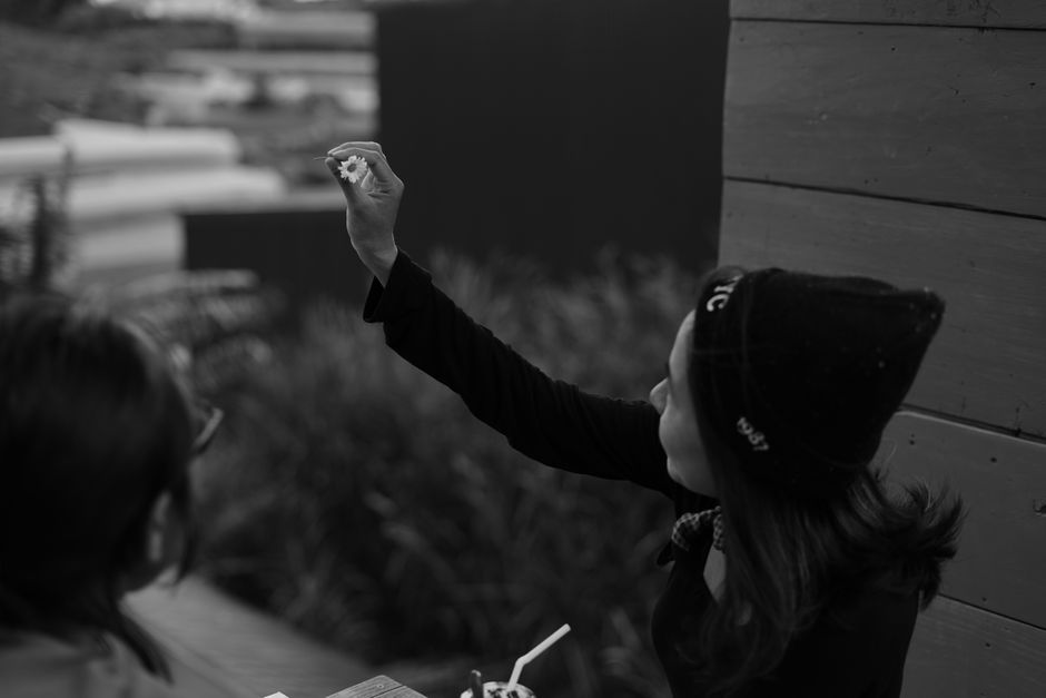 A woman in a cozy beanie holds a flower outdoors in Dalat, capturing a candid moment.