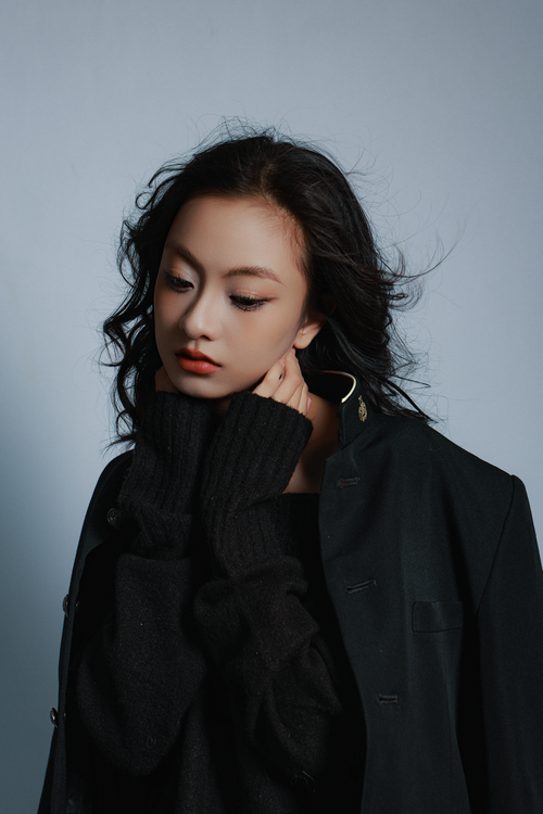 Free Portrait of a young woman in a dark sweater with pensive expression. Soft lighting creates an elegant mood. Stock Photo