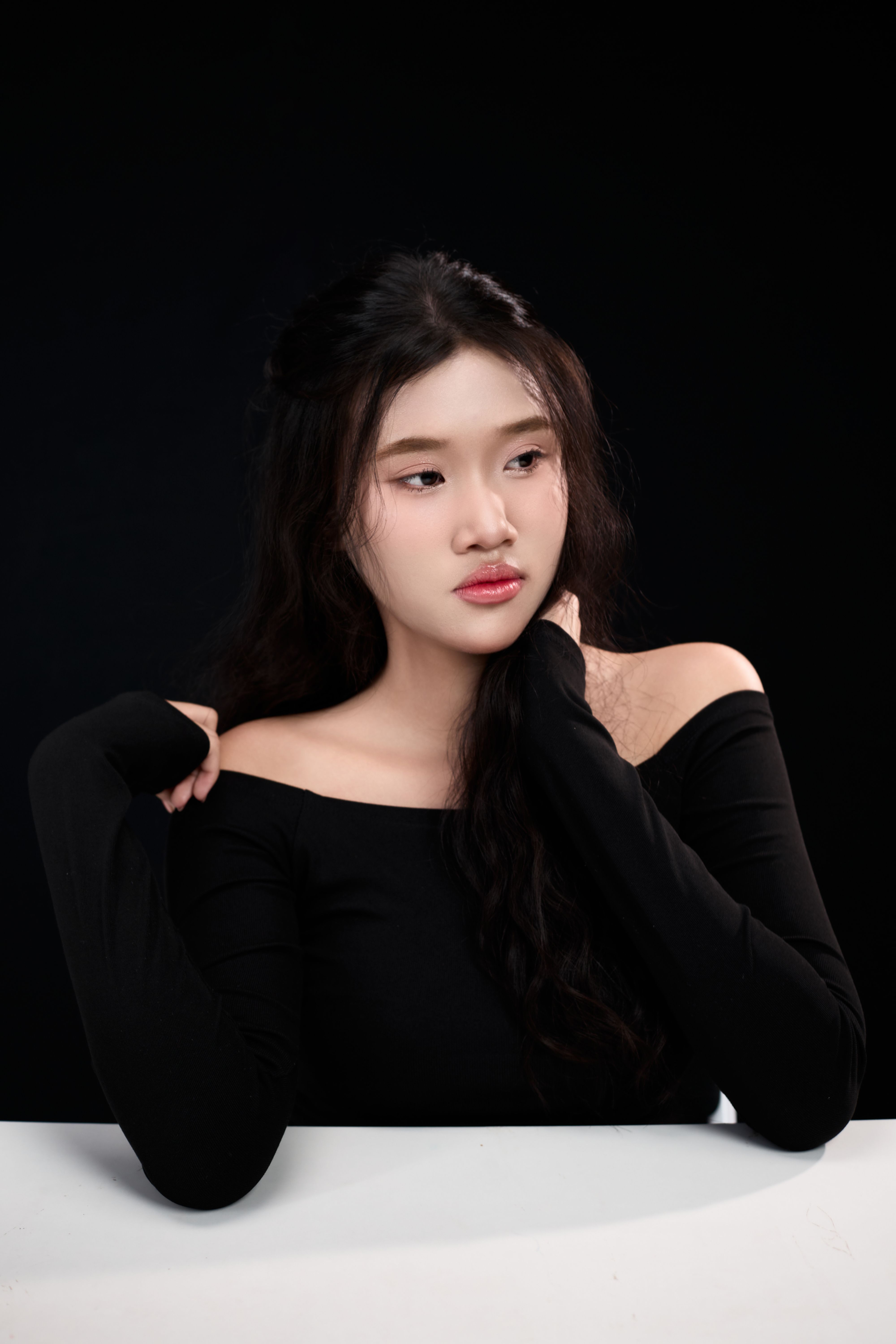 A young woman in a black outfit poses gracefully against a dark background.